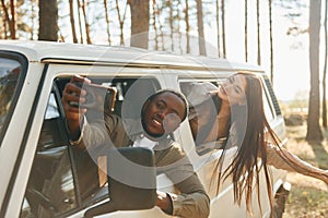 Sitting in the car. Young couple is traveling in the forest at daytime together