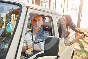 Sitting in the car. Young couple is traveling in the forest at daytime together