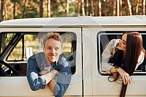 Sitting in the car. Young couple is traveling in the forest at daytime together