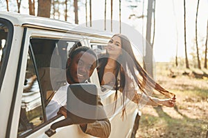 Sitting in the car. Young couple is traveling in the forest at daytime together