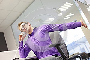 Sitting caucasian man office worker with phone in hand, stretching arm and neck