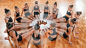 Sitting on circle. Group of female kids practicing athletic exercises together indoors