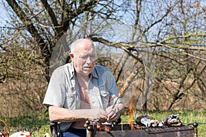 Sitting Elderly Man Roasting Meat at Campground