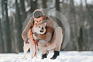 Sitting and embracing the dog. Man having a walk with his akita inu dog outdoors in the park at winter