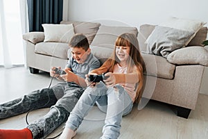 Sitting on the floor and playing videogame. Kids having fun in the domestic room at daytime together