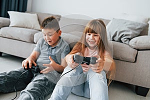 Sitting on the floor and playing videogame. Kids having fun in the domestic room at daytime together