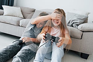 Sitting on the floor and playing videogame. Kids having fun in the domestic room at daytime together