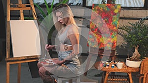 Sitting in front of canvas on chair woman with pelette and paintbrush