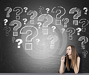 Sitting girl and question marks on blackboard
