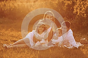 Sitting on the grass. Father, mother with daughter and son spending free time outdoors at sunny day time of summer