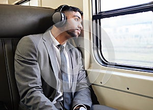 Sitting with his thoughts for a bit. a young businessman wearing headphones while staring out the window on a train