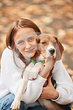 Sitting, holding animal and looking into the camera. Young woman is with her dog in the park