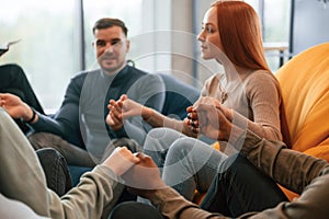 Sitting and holding each other by hands. Group of people are having therapy meeting together