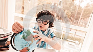 Sitting Little Boy in Glasses Studying Globus.