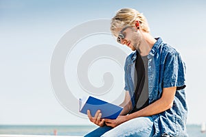 Sitting man reading book outside on sunny day