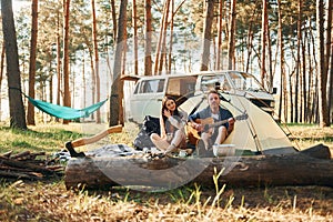 Sitting near the tent. Young couple is traveling in the forest at daytime together