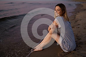 Sitting: Portrait of a Beautiful blonde woman in a light blue dress on the Baltic Sea beach during sunset with vivid