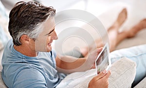 Sitting and relaxing on the couch. a handsome mature man using a tablet while sitting on his living room sofa.