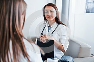 Sitting and talking. Young woman have a visit with female doctor in modern clinic