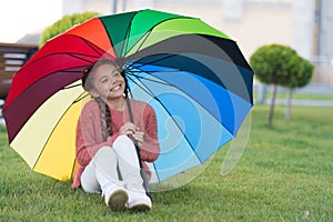 Sitting under umbrella and having fun. Small girl in park waiting for rain. Colourful umbrella as concept of happiness