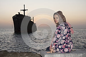 Sitting woman with greek ship wreckage in kish island after sunset