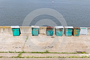 Six (6) green garbage containers standing on the stone embankmen