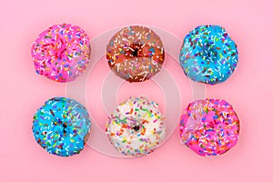 Six assorted donuts with pastel icing against a soft pink background