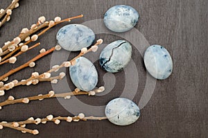 Six blue marble eggs, painted in hibiscus tea, with willow branches lie on black background