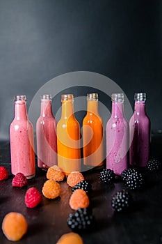 Six bottles with smoothies and raspberry, (red, yellow, blackberry) on black background. Milk shake in glass jar with berries. die
