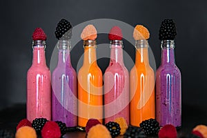 Six bottles with smoothies and raspberry, red, yellow, blackberry on black background. Milk shake in glass jar berries. diet or