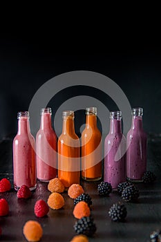 Six bottles with smoothies and raspberry, red, yellow, blackberry on black background. Milk shake in glass jar berries. diet or v