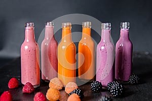 Six bottles with smoothies and raspberry, red, yellow, blackberry on black background. Milk shake in glass jar berries. diet or v