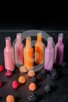 Six bottles with smoothies and raspberry, red, yellow, blackberry on black background. Milk shake in glass jar berries. diet or v