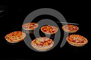 Six burnt homemade mini pizzas on tray in electric oven, black background