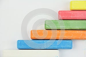 Six colored children crayons on white background, on right side, blue red green yellow orange white, top view