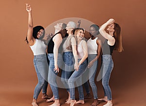 Six diverse women laughing together. Females with different body types having fun while standing against a brown background