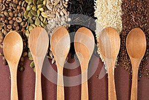 Six empty wooden spoons on a surface of different seeds and brown background