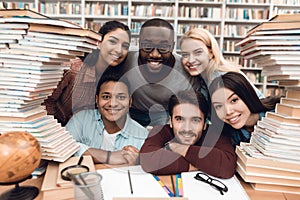 Six ethnic students, mixed race, indian, asian, african american and white surrounded with books at library.