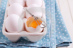 Six fresh eggs in egg holder with one cracked egg