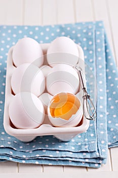 Six fresh eggs in egg holder with one cracked egg