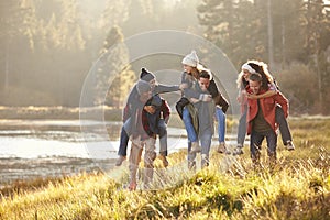 Six friends have fun piggybacking in the countryside by lake