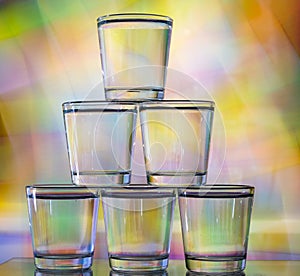 Six glasses stacked by a tower on a multi-colored background