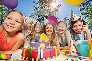 Six happy kids in party hats around birthday cake