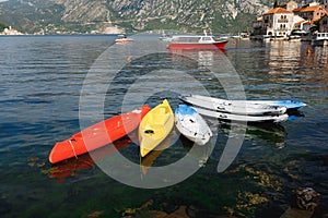 Six kayaks moored near the shore in city of Perast, Montenegro. Kayak red, yellow, white-blue