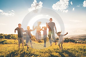 Six kids brothers and sisters teenagers and little kids jumping on a green grass meadow with evening sunset background light