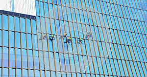 Six men workers in red and yellow work clothes cleaning the exterior windows of a business skyscraper - industrial