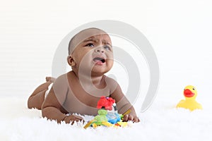 A six month crawling African American baby playing with yellow duck toy on fluffy white rug, happy smiling adorable sweet little