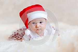 six-month-old baby girl with big beautiful eyes in red santa cap lies on her stomach for Christmas. Photo shoot babies