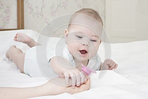 The six-month-old baby girl lies on her stomach and pulls her hand to the nipple. A small child in white looks at the pacifier.