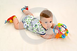 The six-months baby holds a toy on a light background, the top view